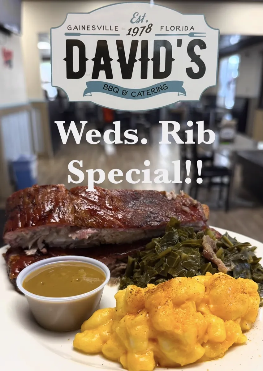 A rack of ribs with collards, mac and cheese, and a cup of mustard sauce, under the David's BBQ and Catering plaque with the words Weds. Rib Special across it