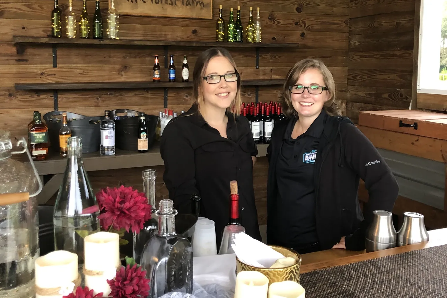 A bartender behind a candlelit bar dressed with flowers and bottles.