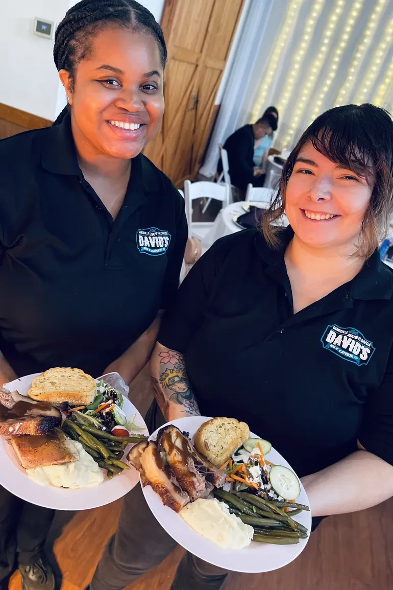 Two team members in David's polos presenting plated dinners