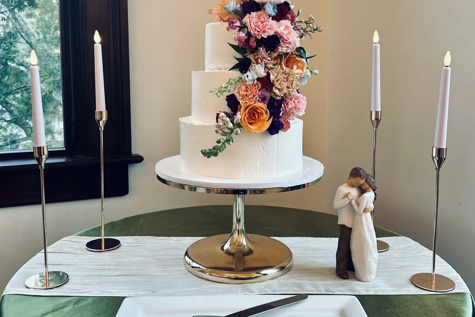 Three tier cake with cascading roses beside a figurine