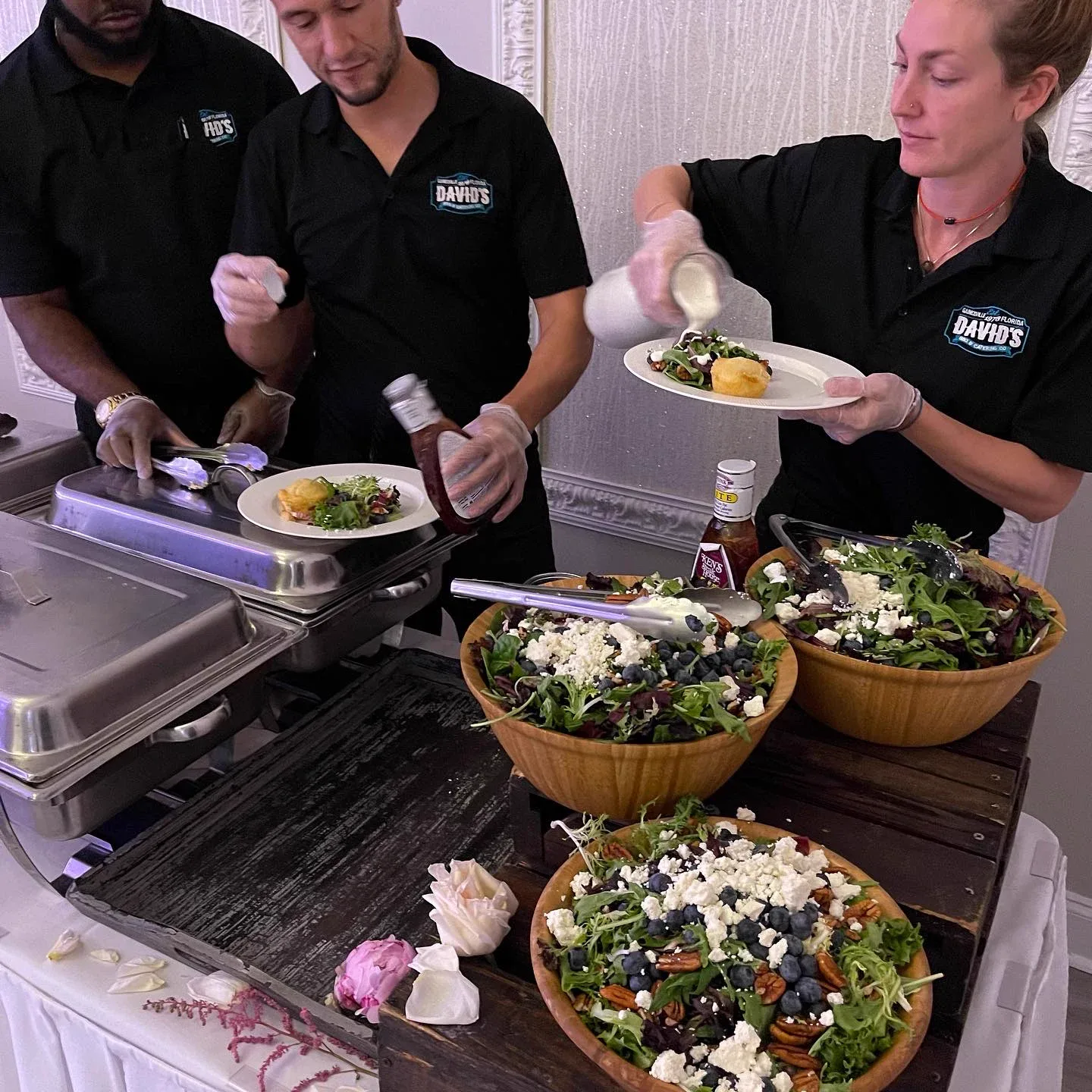 Two staff members serving salad from large wooden bowls