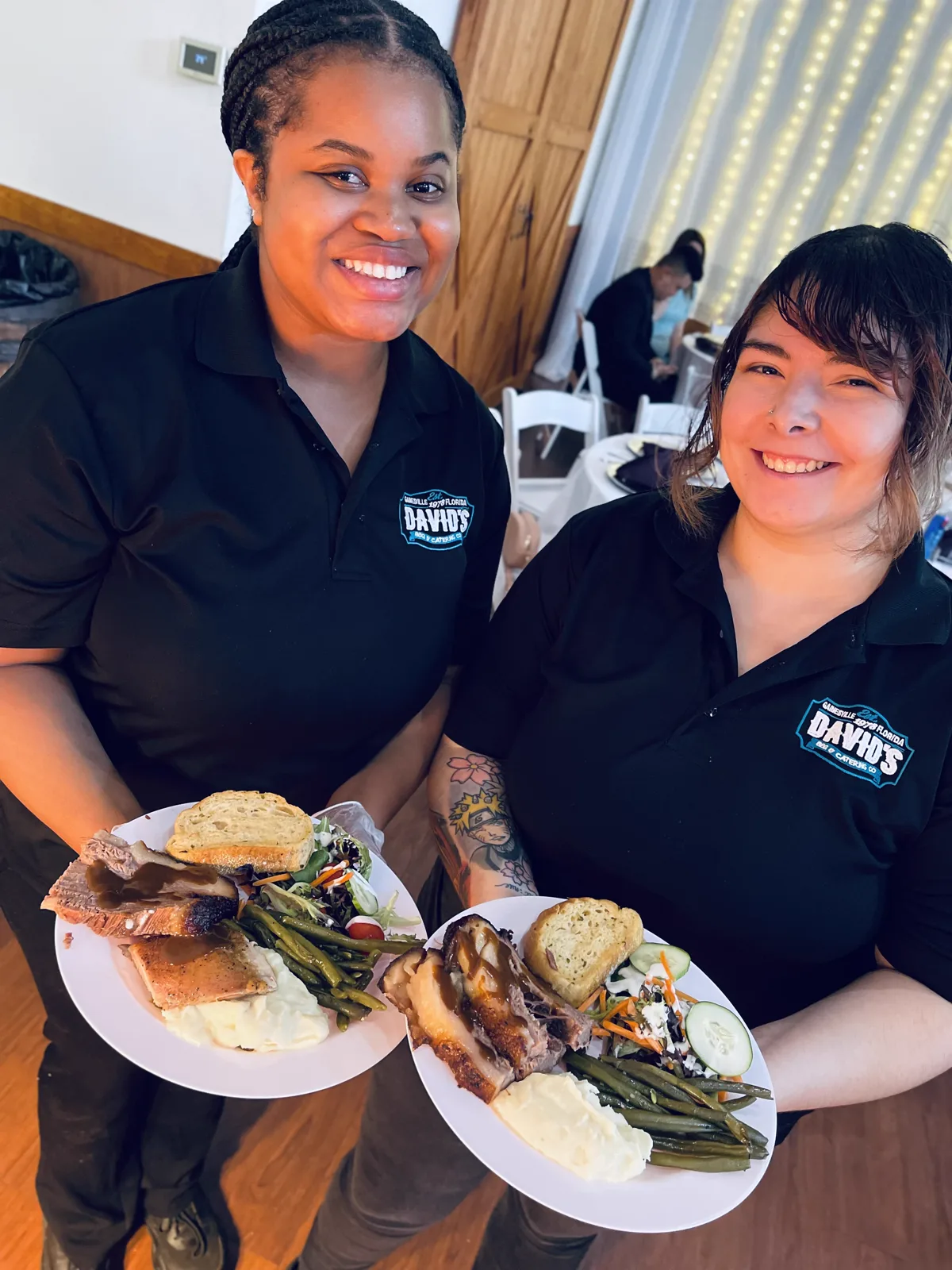 Two catering staff holding plated dinners