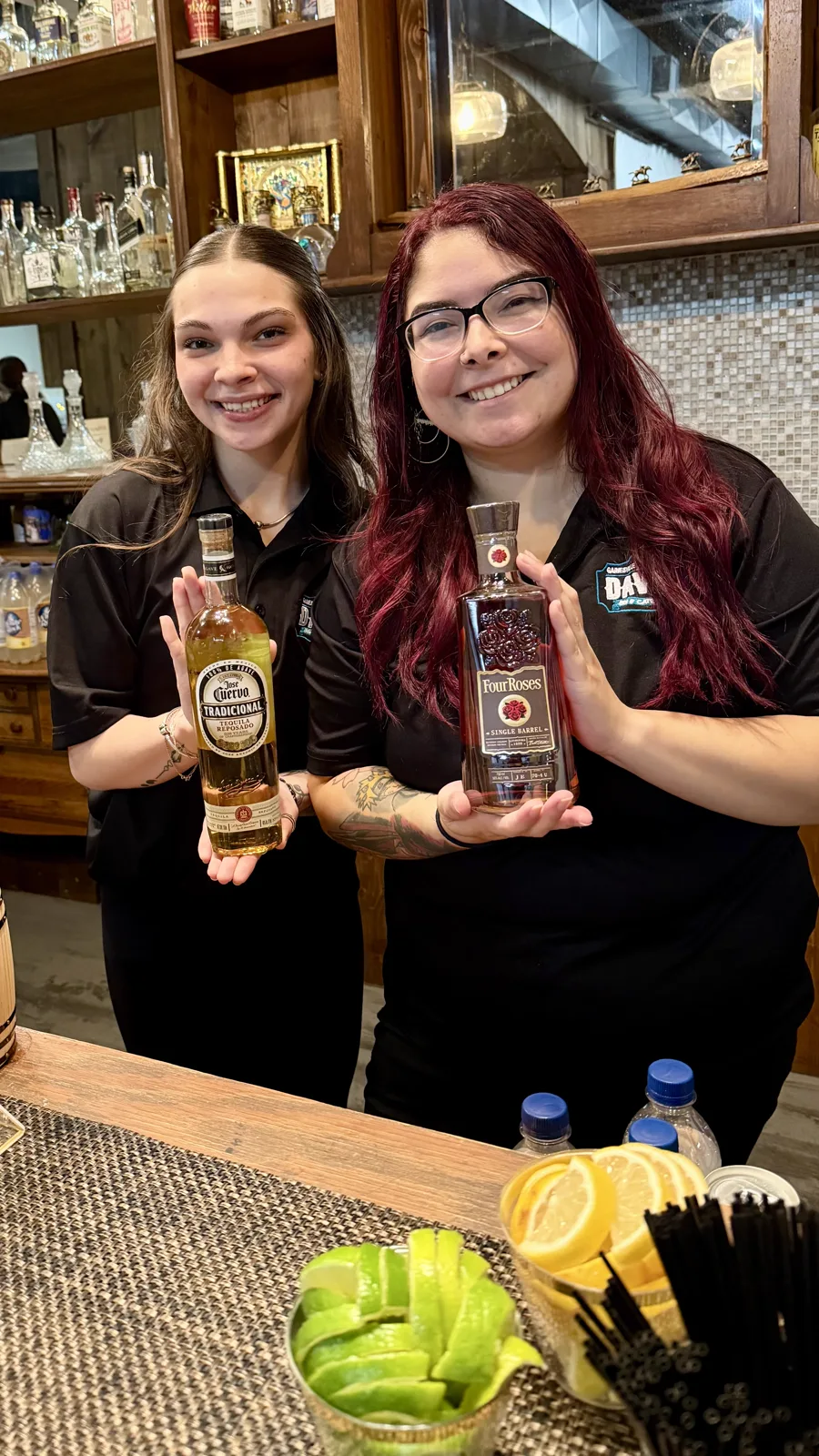 Two bartenders holding bottles behind the bar