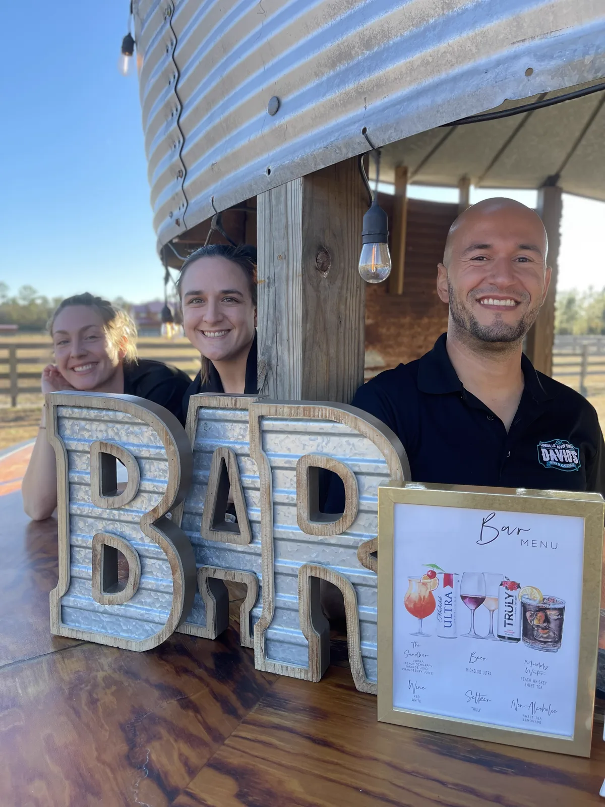 Three staff members beside oversized marquee BAR letters