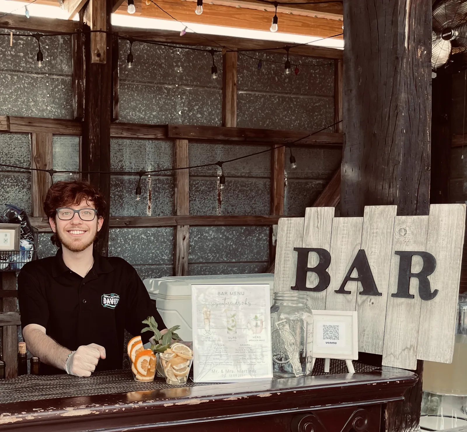 A bartender at a rustic bar beneath a wooden BAR sign
