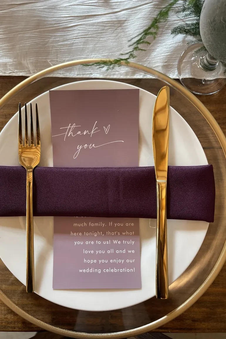 Gold flatware and a thank you card on a burgundy napkin