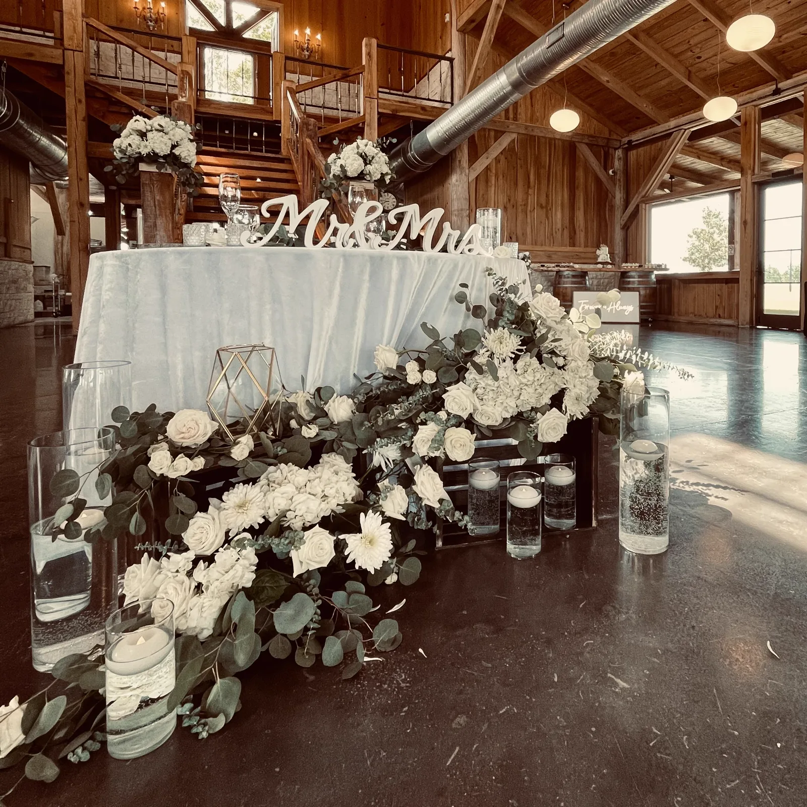 A sweetheart table banked with white florals beneath a Mr and Mrs sign