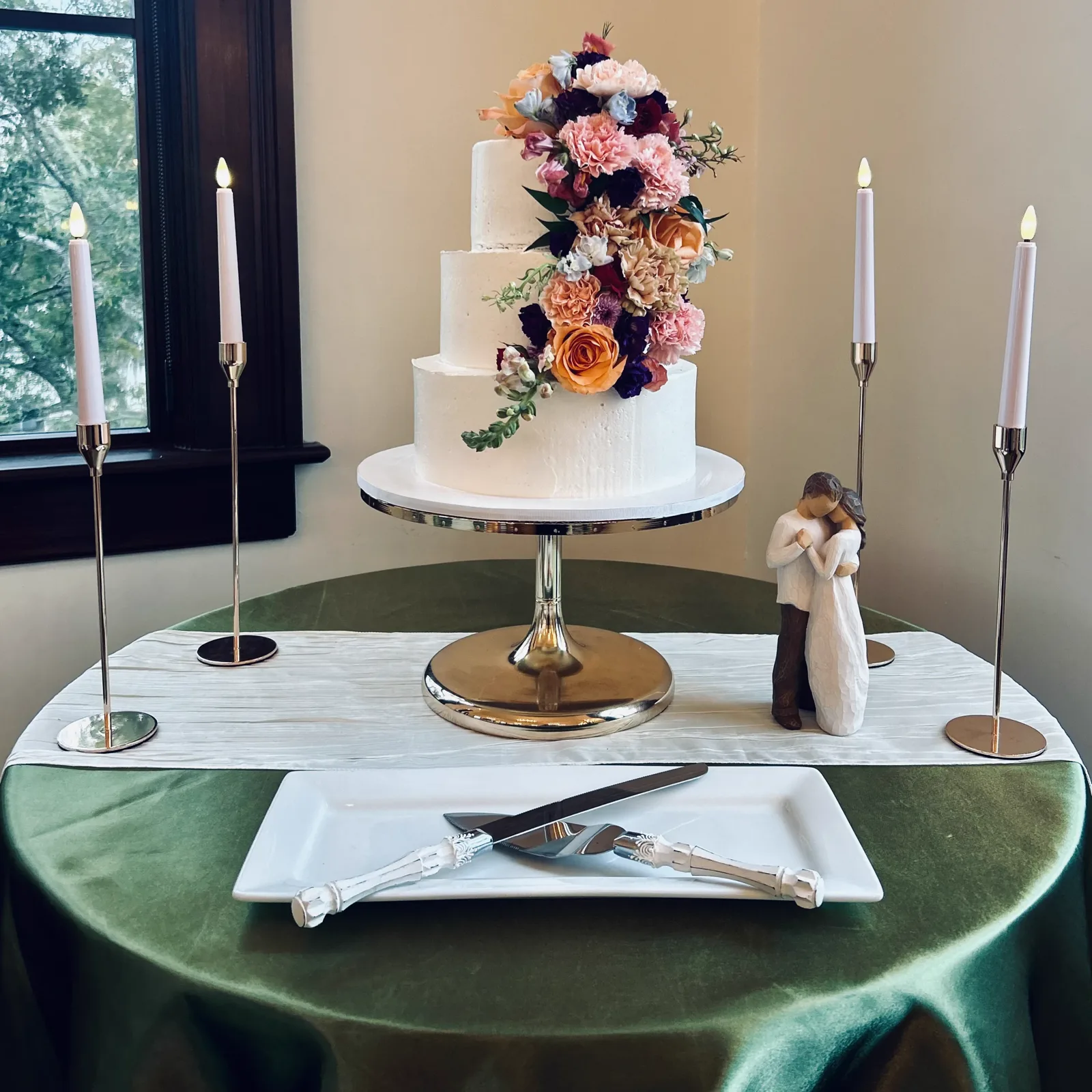 A white wedding cake topped with florals on a green velvet table