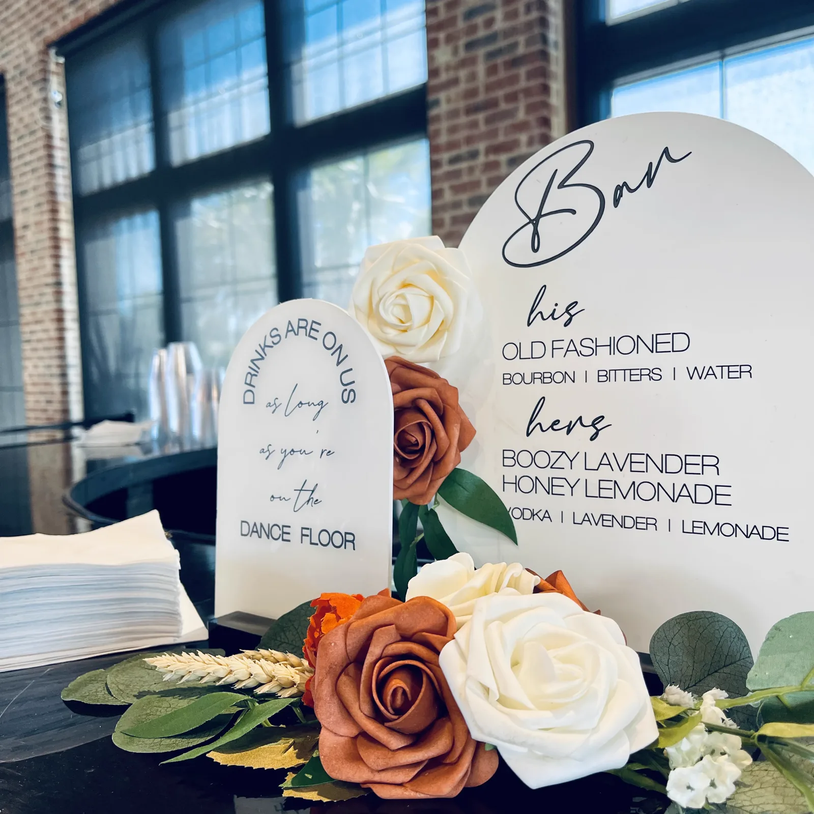 A bar menu sign listing his and hers cocktails beside roses
