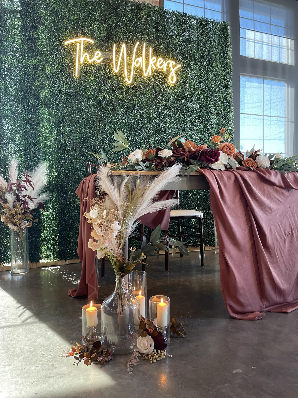 A neon family name sign on a greenery wall above draped fabric