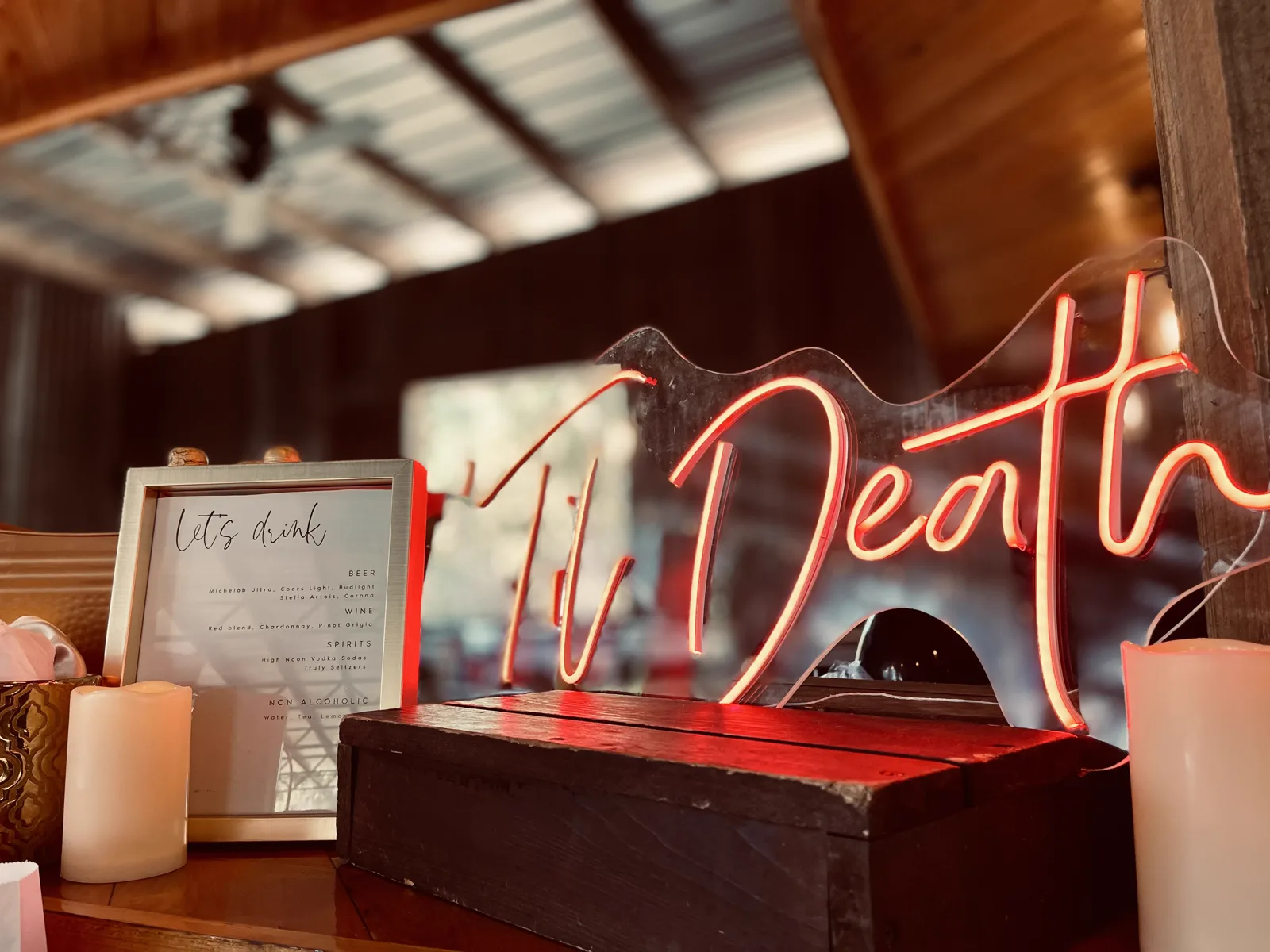 A Til Death neon sign glowing above candles on a wooden bar