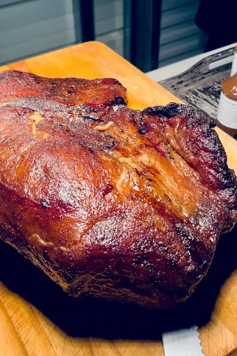 Burnished smoked pork shoulder resting on a carving board.