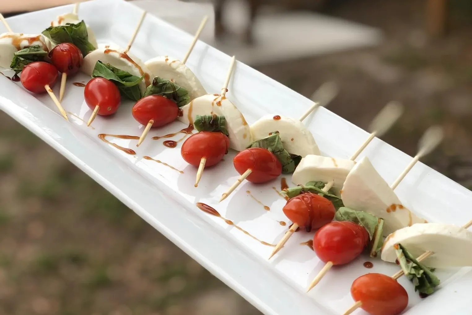 Caprese skewers drizzled with balsamic on a white platter