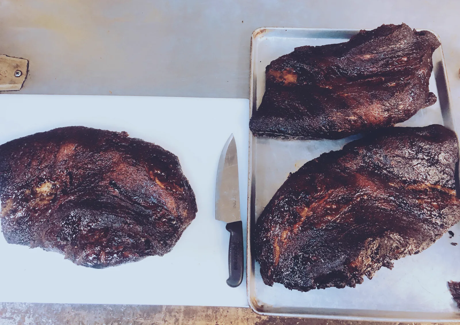 Two whole smoked briskets resting on a carving board beside a knife