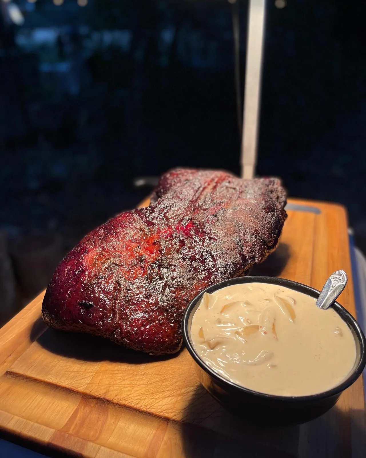 A smoked pork roast on a wooden board with a bowl of sauce