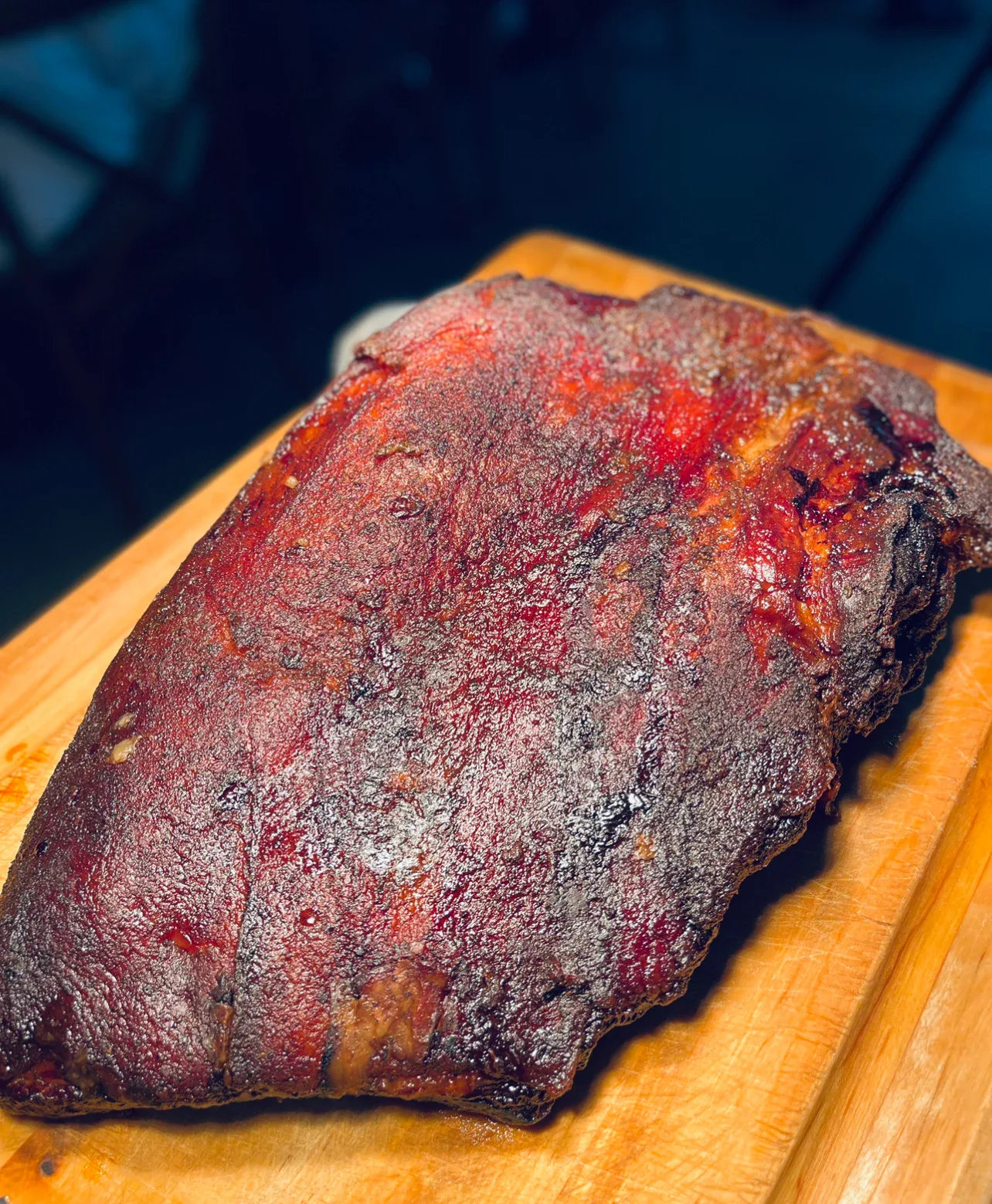A dark-barked brisket on a carving board under warm light