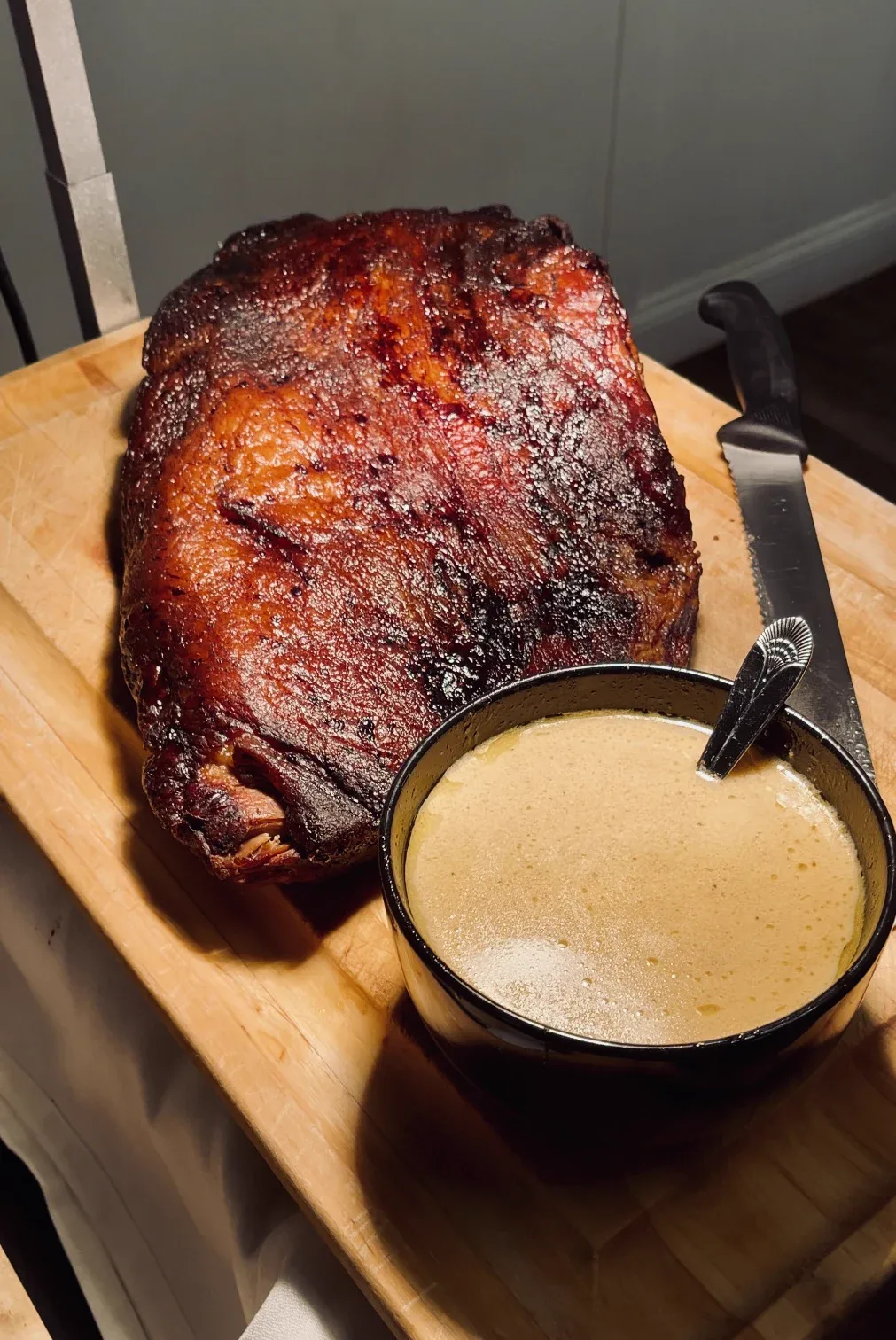 A glazed smoked ham on a board beside a bowl of sauce