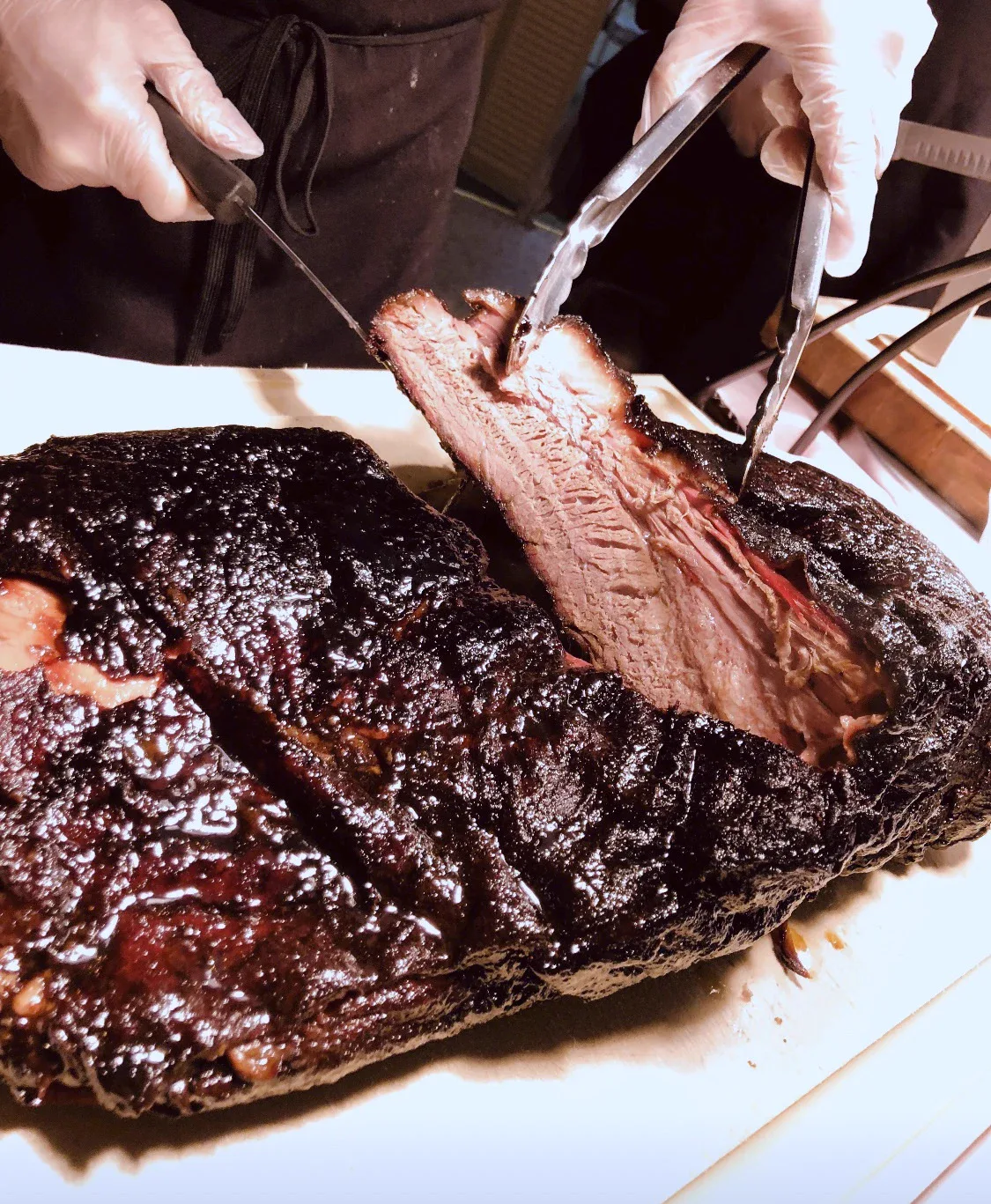 Gloved hands slicing into a smoked brisket with a carving knife