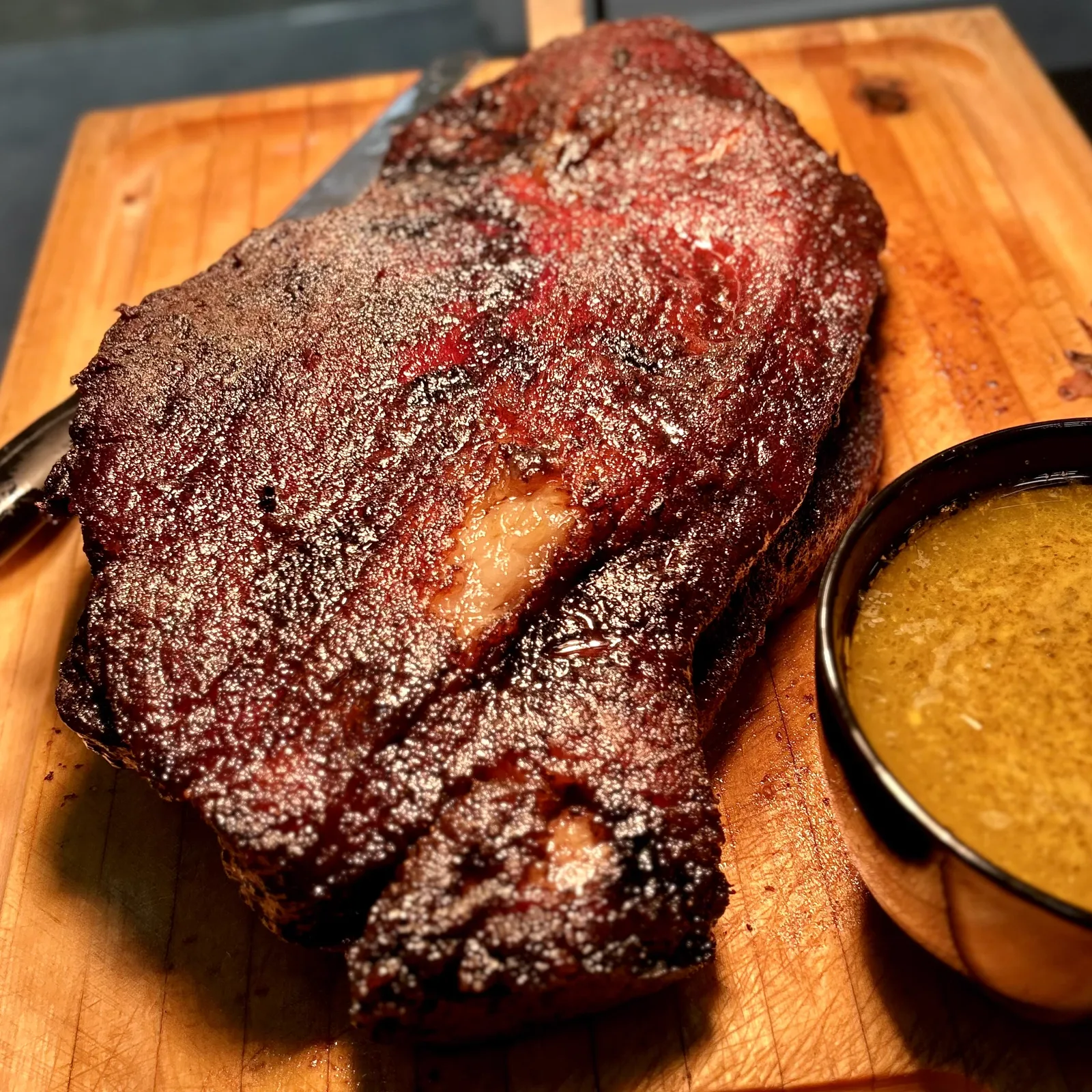 A peppered smoked roast on a board beside a bowl of mac and cheese
