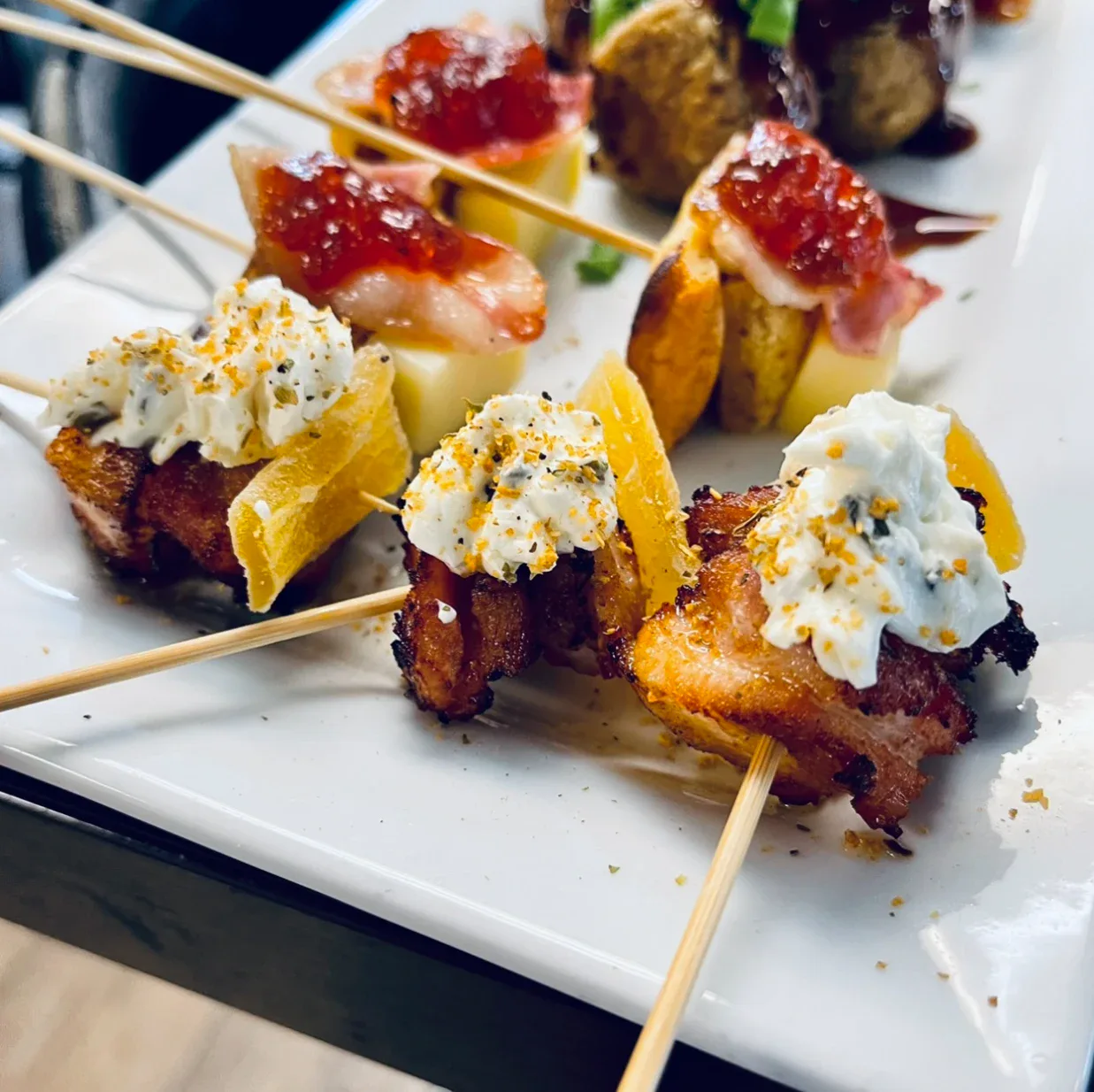 Bacon-wrapped skewers topped with cream and preserves on a white platter
