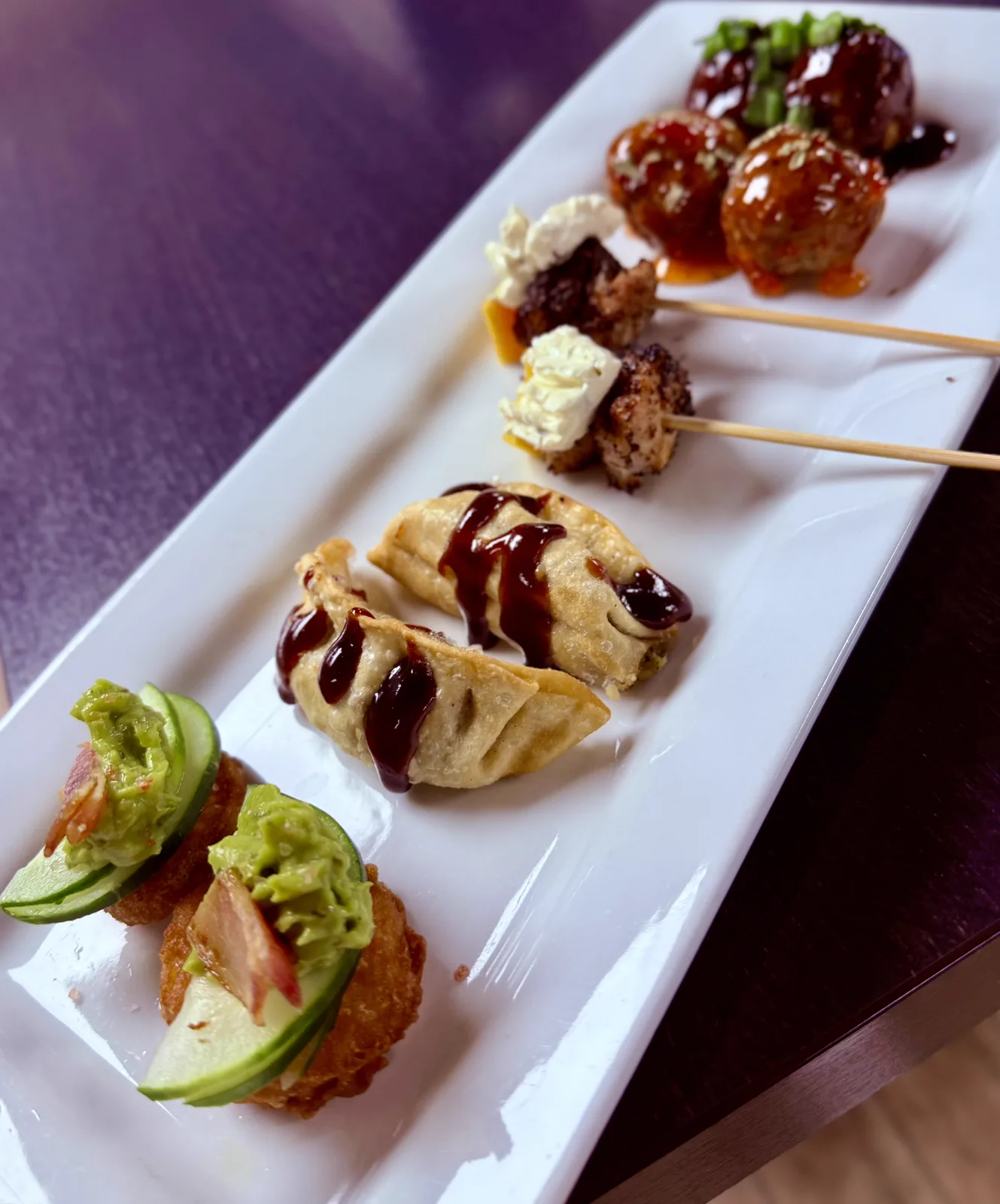 A long white platter of skewered appetizers with avocado and chili glaze