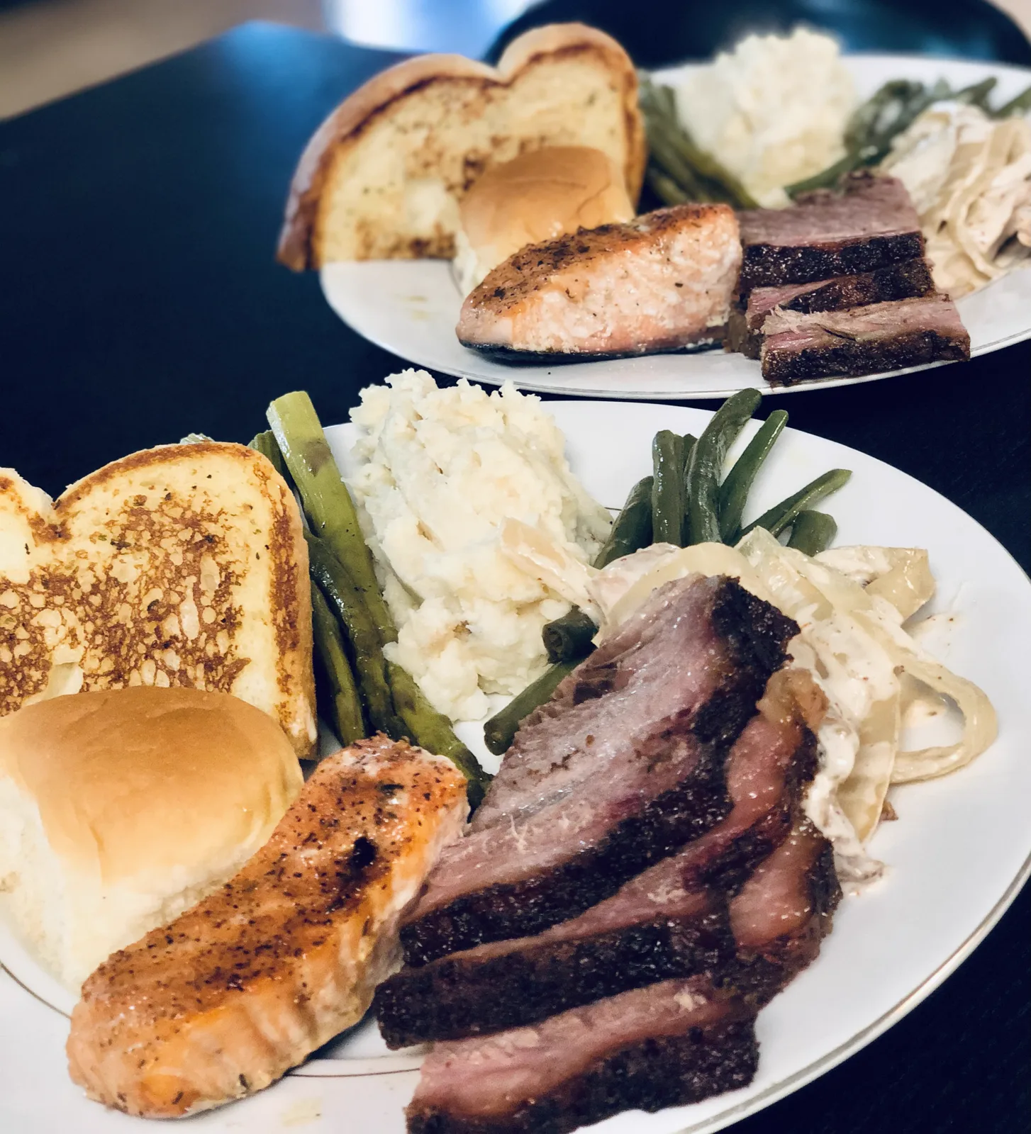 A plate of salmon, brisket, green beans and garlic toast