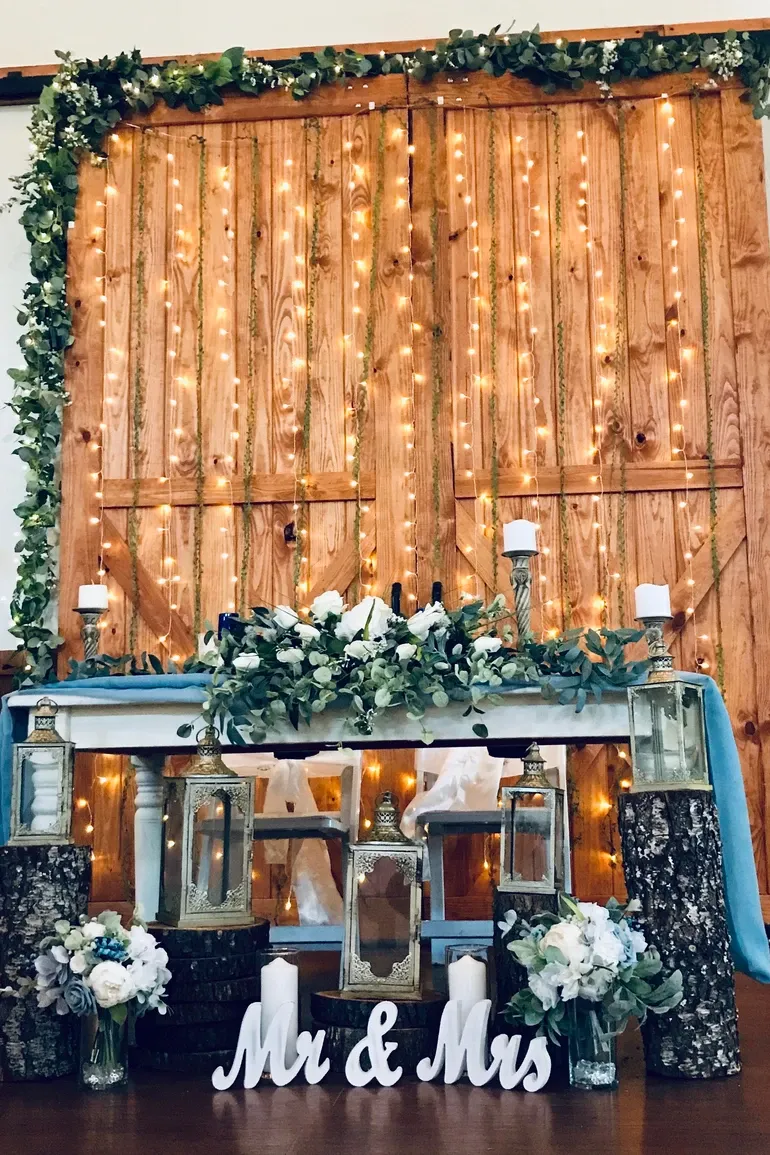 Barn doors wrapped in string lights behind a greenery head table