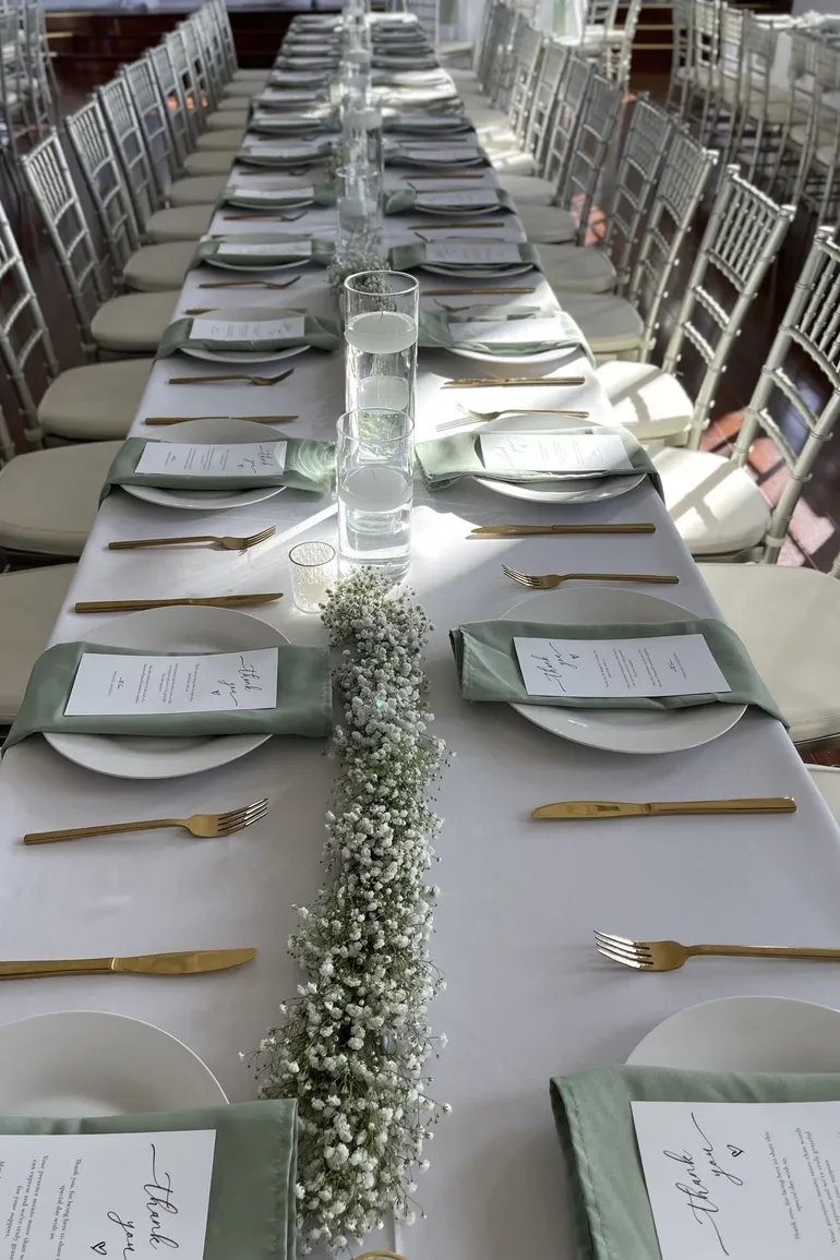 Long reception table with sage runners, menus, and gold chiavari chairs