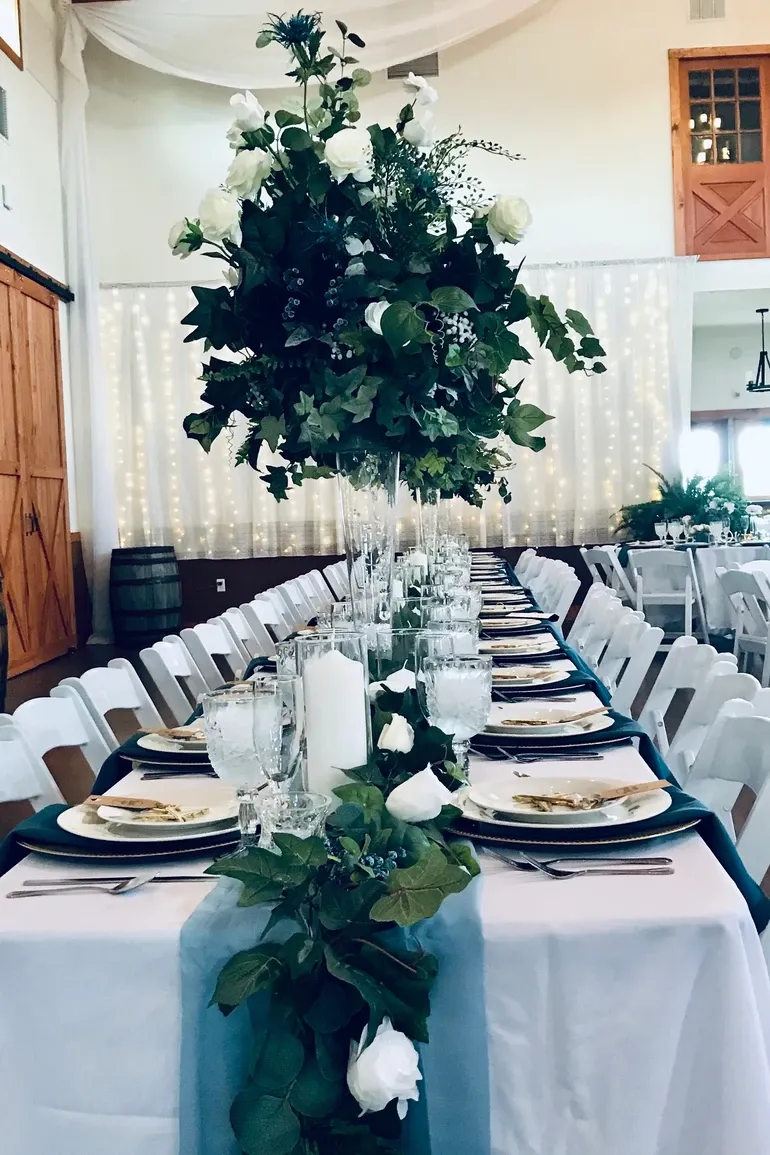 Long royal table with tall greenery centerpieces under curtain lights.