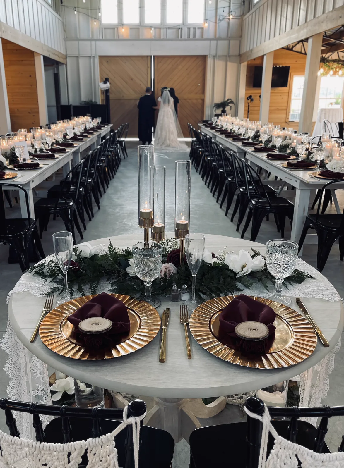 Long banquet tables with black chairs set for a barn reception