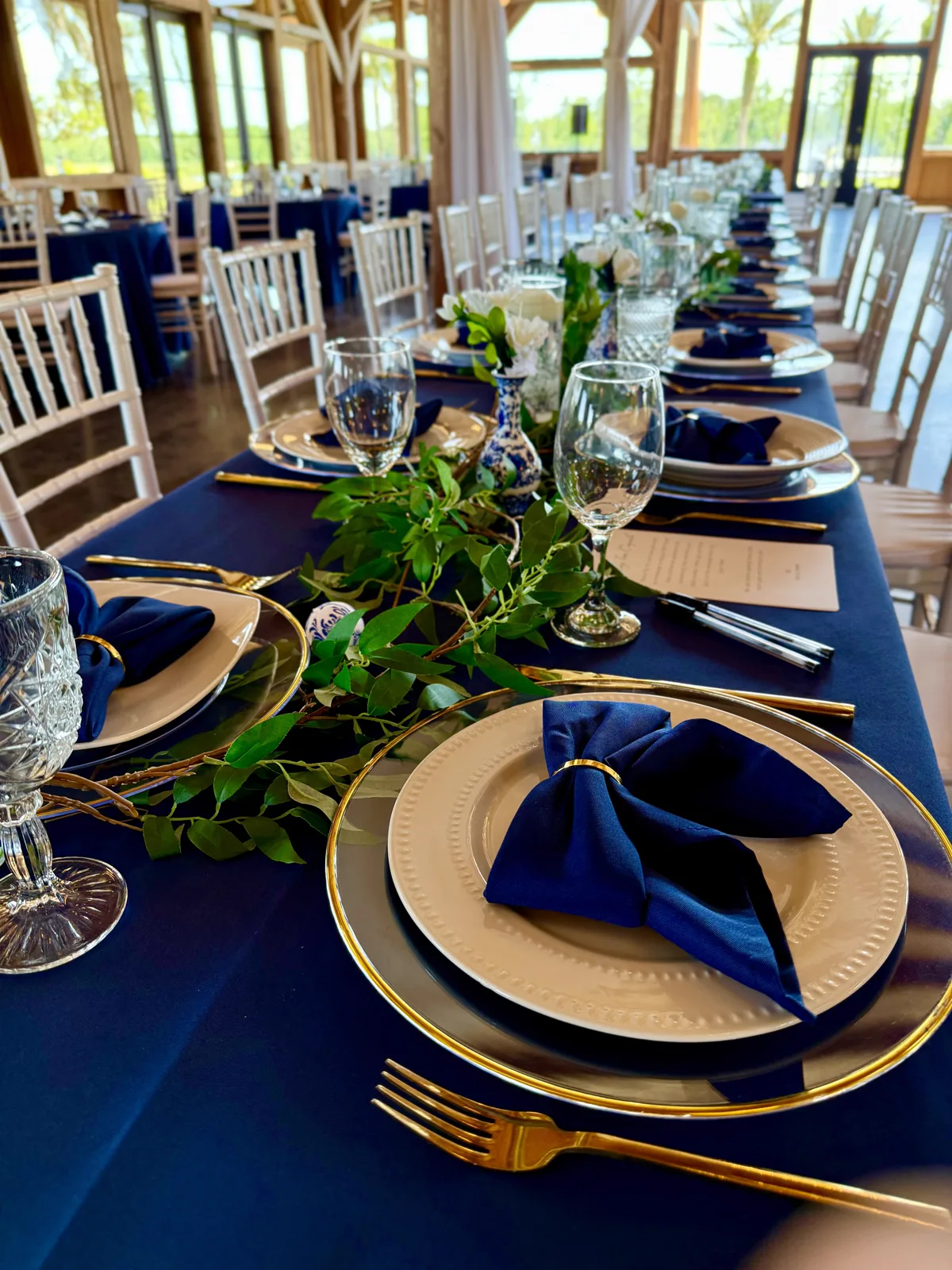 A navy reception table with gold chargers and trailing greenery