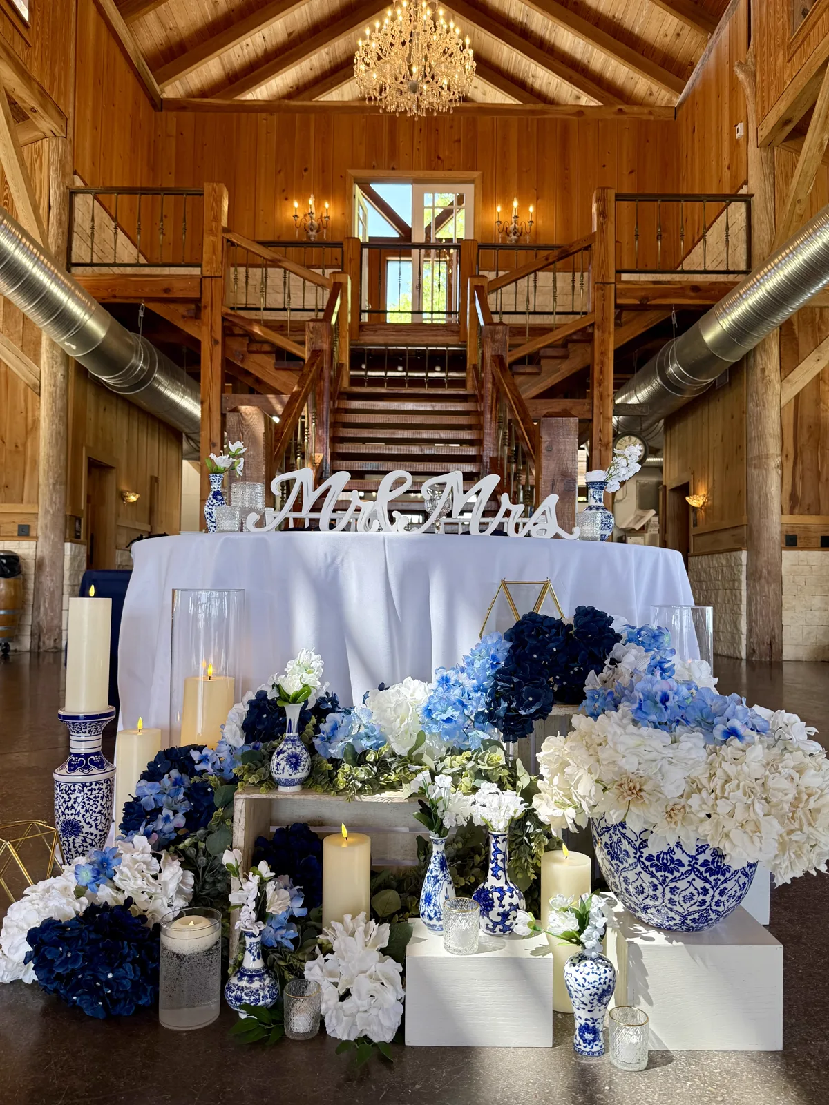 A sweetheart table with blue and white florals beneath a barn staircase