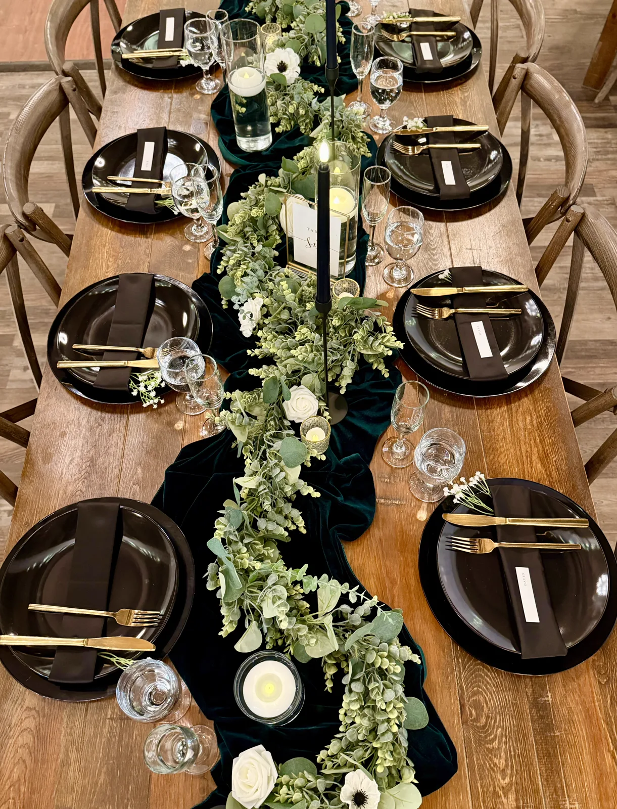 Dark place settings along a greenery runner on a wooden table