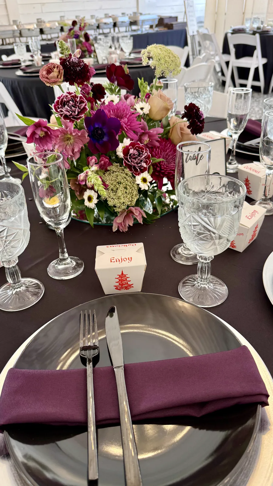 A round table with a tall floral centerpiece and plum napkins