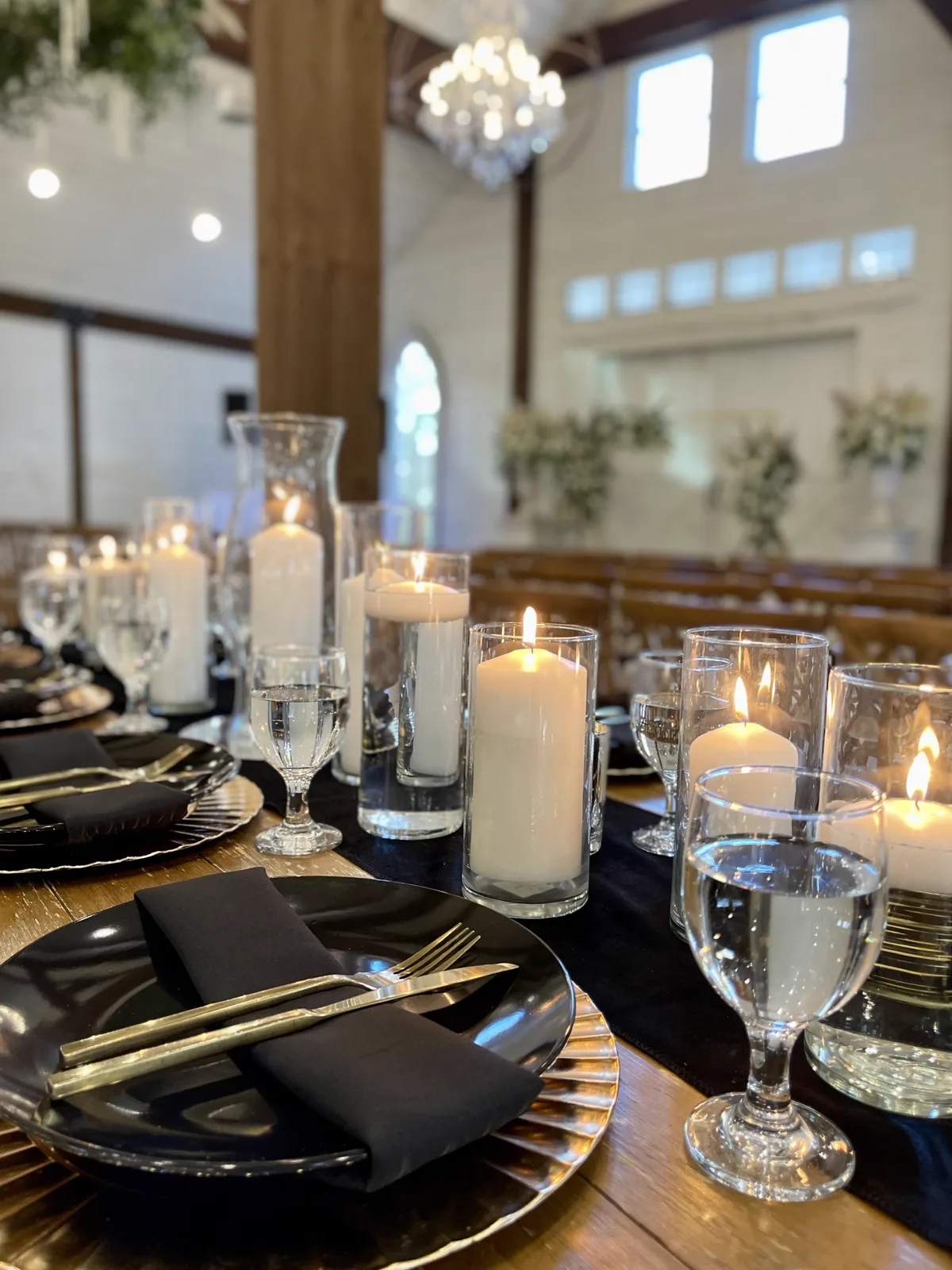 A long table set with black chargers, candles and glassware