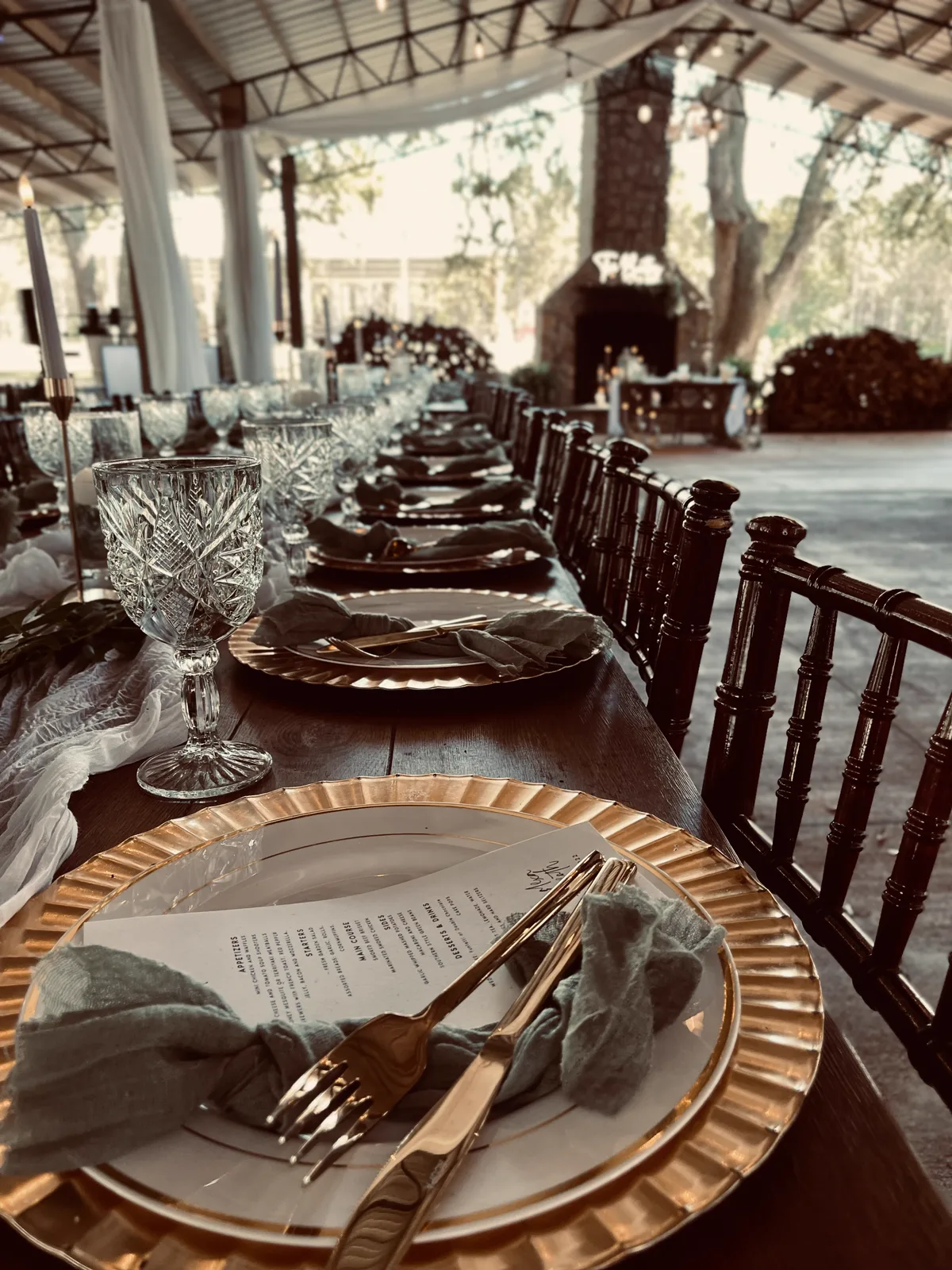Gold chargers and printed menus along a table under a pavilion