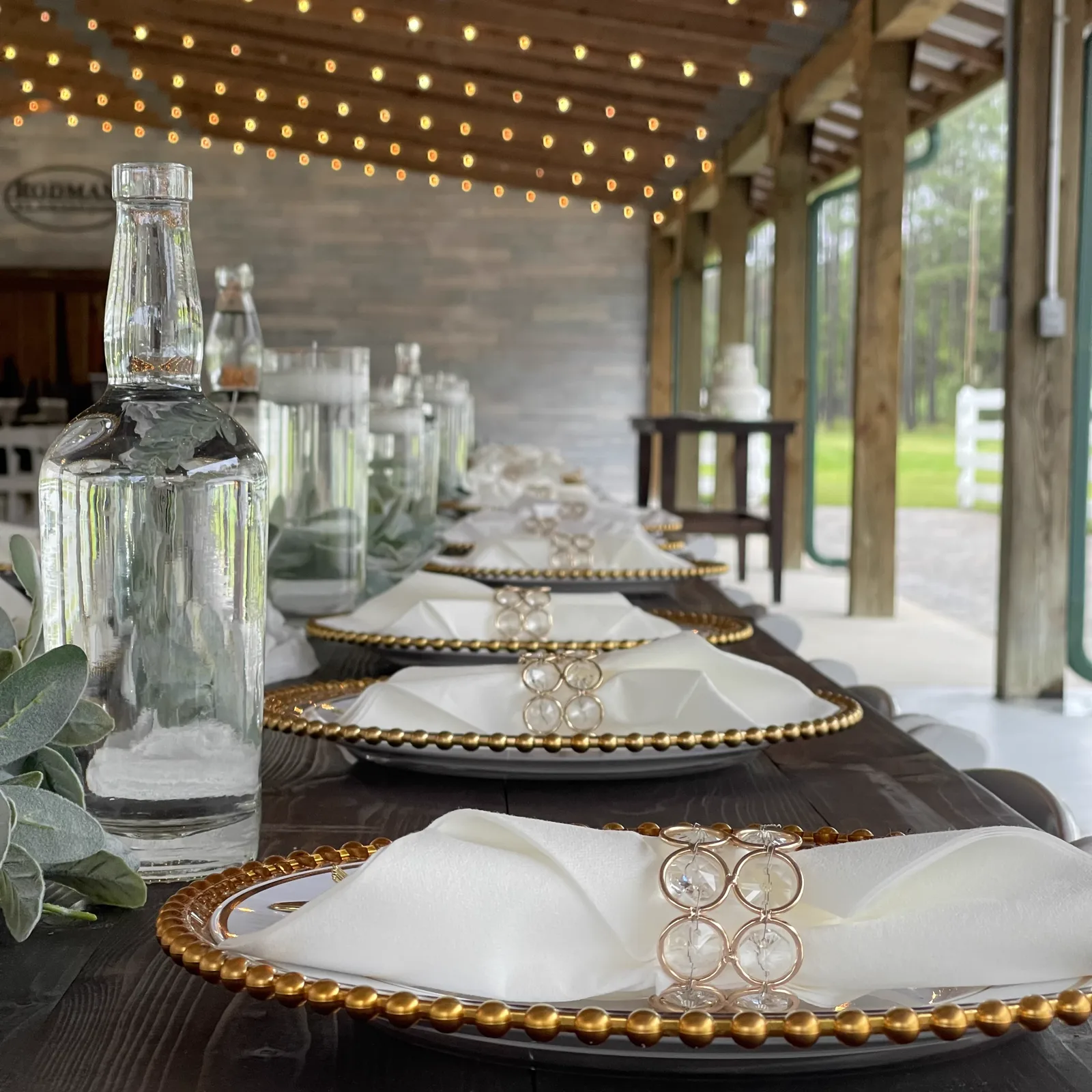 White chargers and glassware on a table beneath string lights