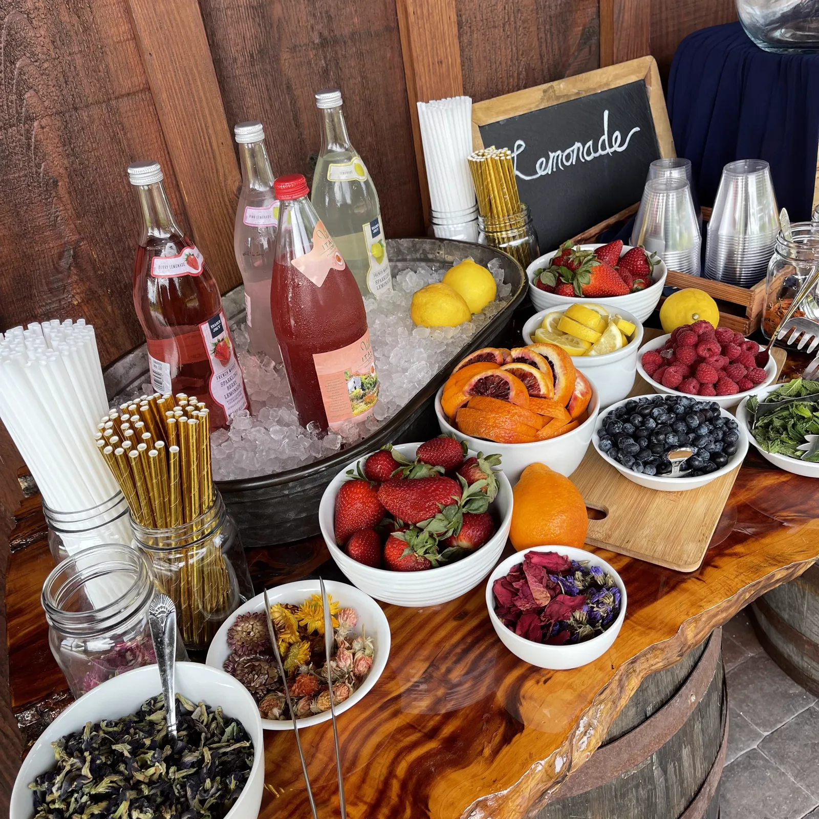 A drink station with bottles, fresh fruit and garnishes on a wooden table