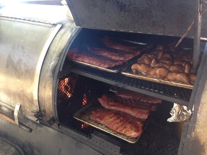 The offset smoker loaded with racks of ribs and chickens over a live fire.