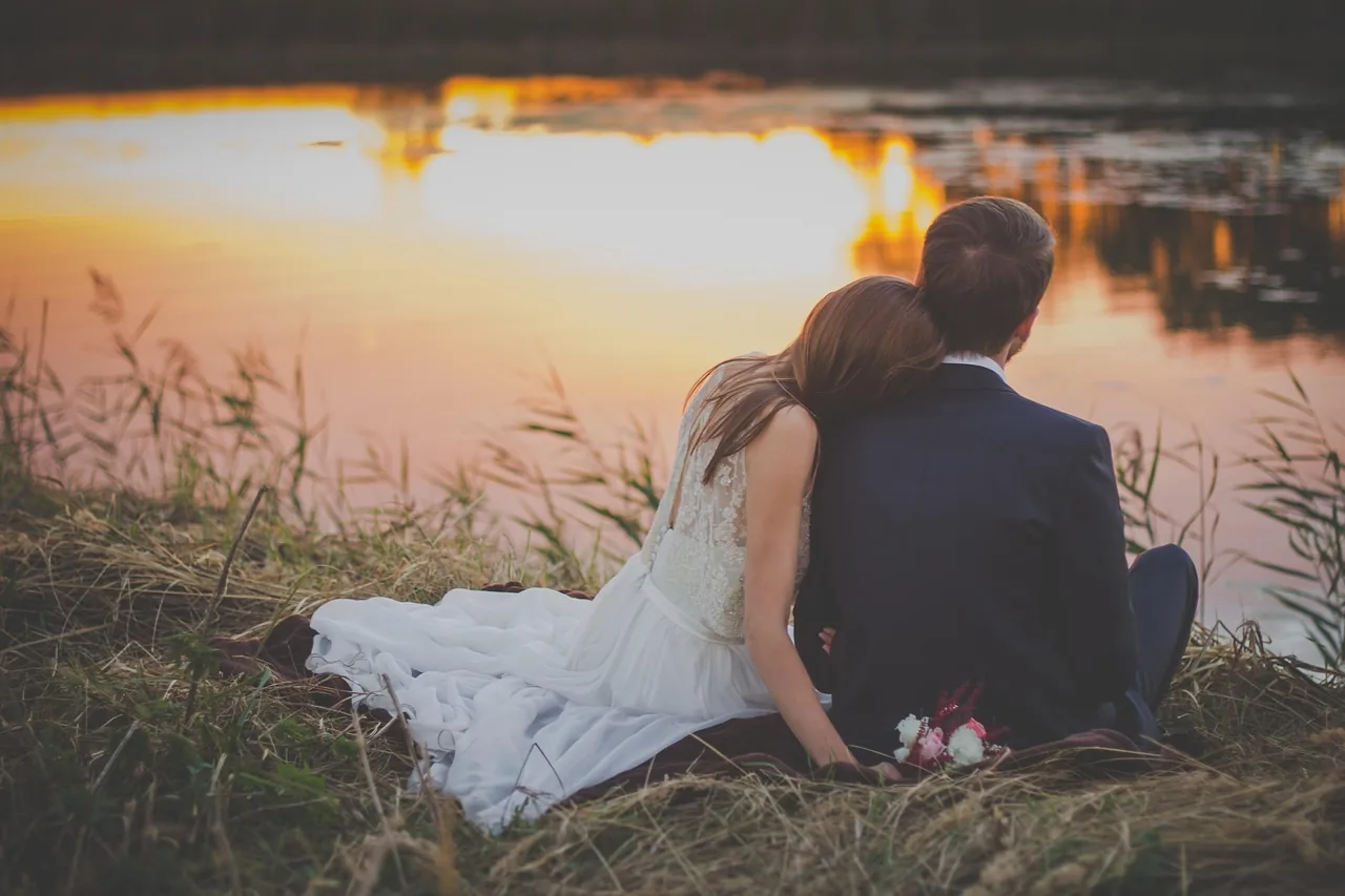 A couple seated at the edge of still water at sunset.